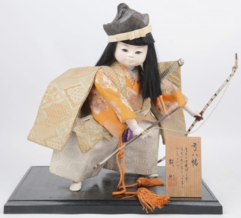 “Boogschutter”. Een Japanse pop met porseleinen hoofdje, handjes en voetjes en met zijden klederdracht.