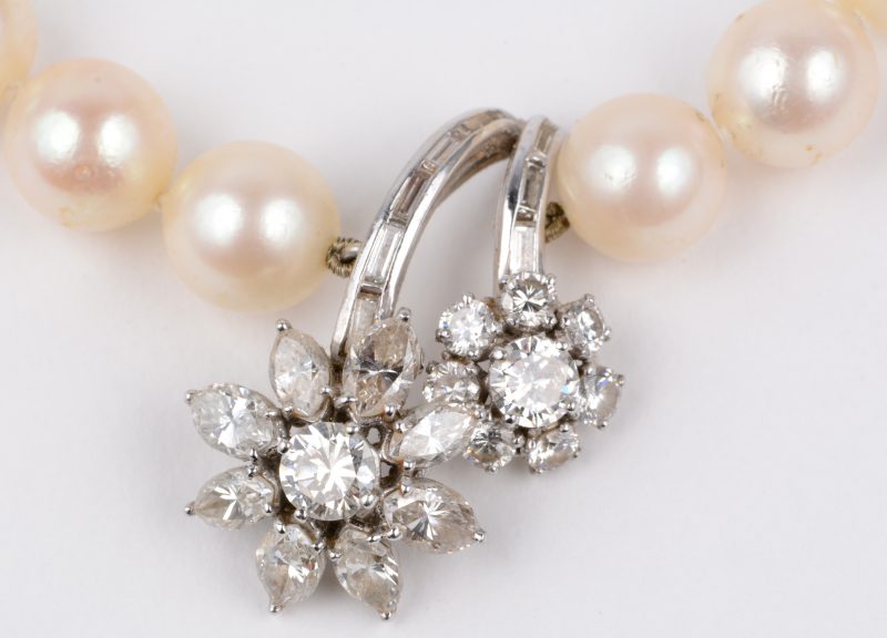 Een parelhalssnoer met 18 karaats wit gouden hanger en slot bezet met diamanten en baguettes met een gezamenlijk gewicht van ± 2,50 ct.