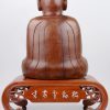 Een zittende Boeddha van gebeeldhouwd hout op een voetstukje, versierd met ingelegde tekens van parelmoer.