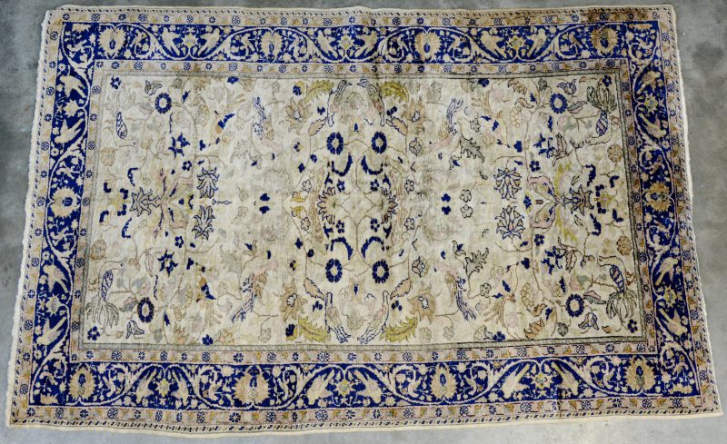 Een handgeknoopt Perzisch karpet met een decor van vogels en bloemen. Slijtage.