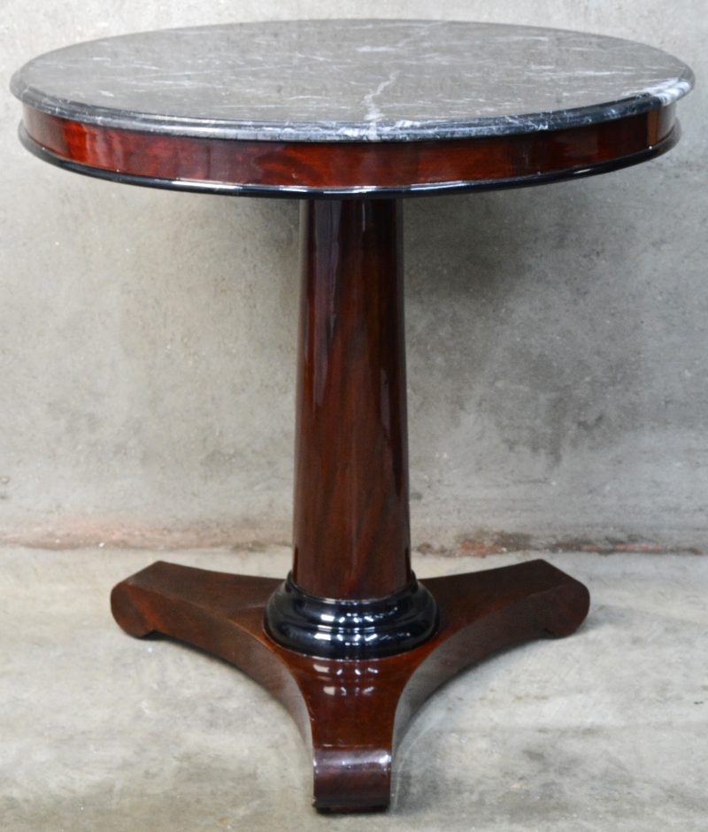 Een gefineerde ronde tafel in empirestijl met een zwart marmeren blad.