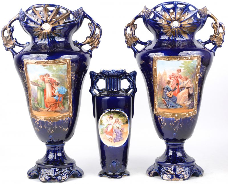Een driedelig kaststel van kobaltblauw en verguld aardewerk met meerkleurige romantische decors.