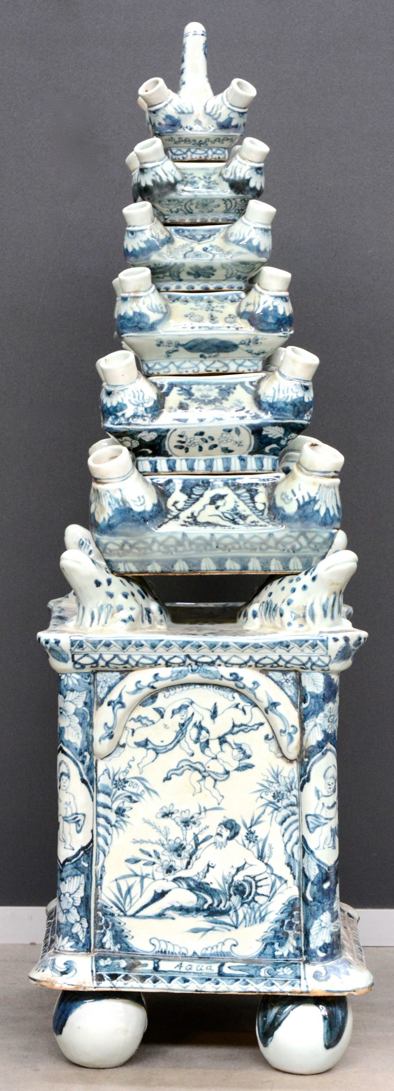 Een grote tulpenvaas, opgebouwd uit zes aflopende componenten, gedragen door vier salamanders op een zware basis. Het geheel versierd met blauw op witte decors.