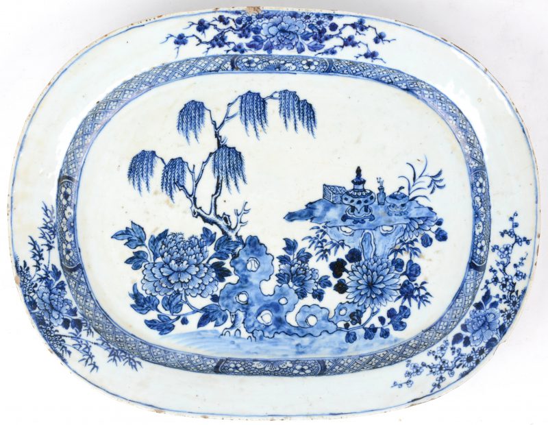 Een schotel van Chinees porselein met een blauw op wit decor van planten en bloemen. Randschilfers.