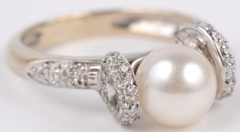 Een 18 karaats wit gouden ring bezet met een briljanten met een gezamenlijk gewicht van ± 0,20 ct. en een parel.