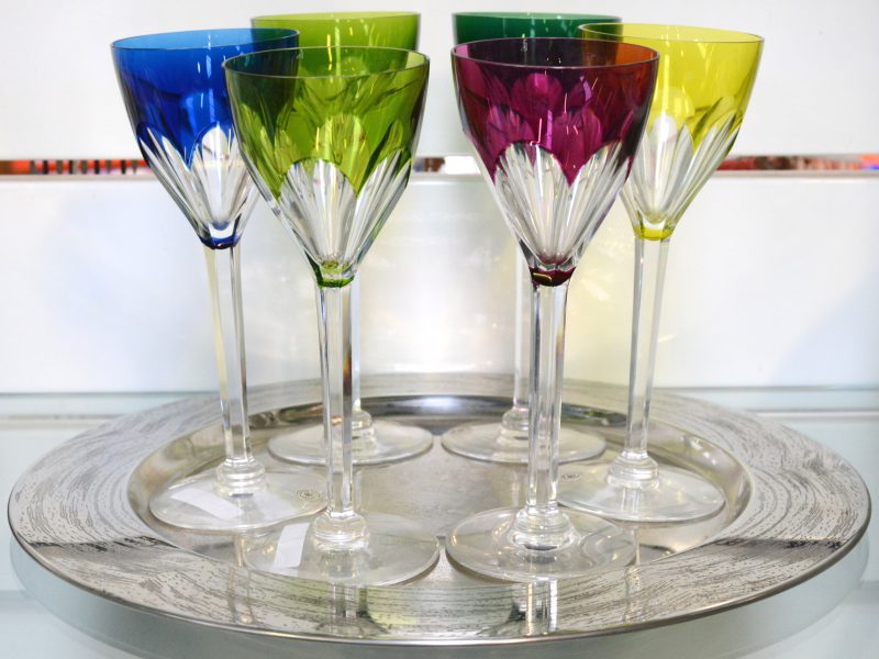 Een serie van zes wijnglazen met diverse kleuren van geslepen kristal. Met merk en label. Gepresenteerd op een verzilverd metalen schotel.
