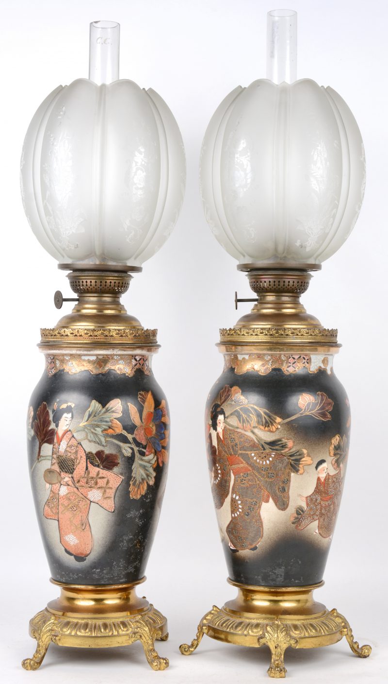 Een paar Satsuma olielampen van aardewerk met koperen monturen. Decor van personages en bloemen. Omstreeks 1900. Compleet met lampenglazen en geslepen en gegivreerde lampenkappen.