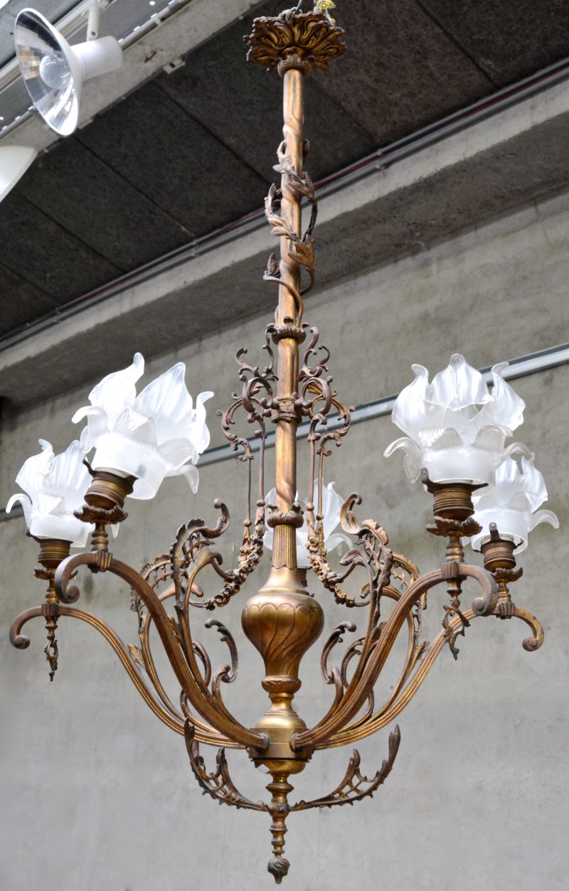 Een bronzen luchter met vier lichtpunten, getooid met bloemvormige glazen kapjes. Begin XXe eeuw.