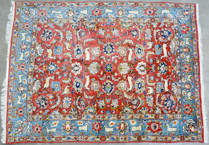 Een handgeknoopt Perzisch wollen karpet met een decor van dieren en bloemen.