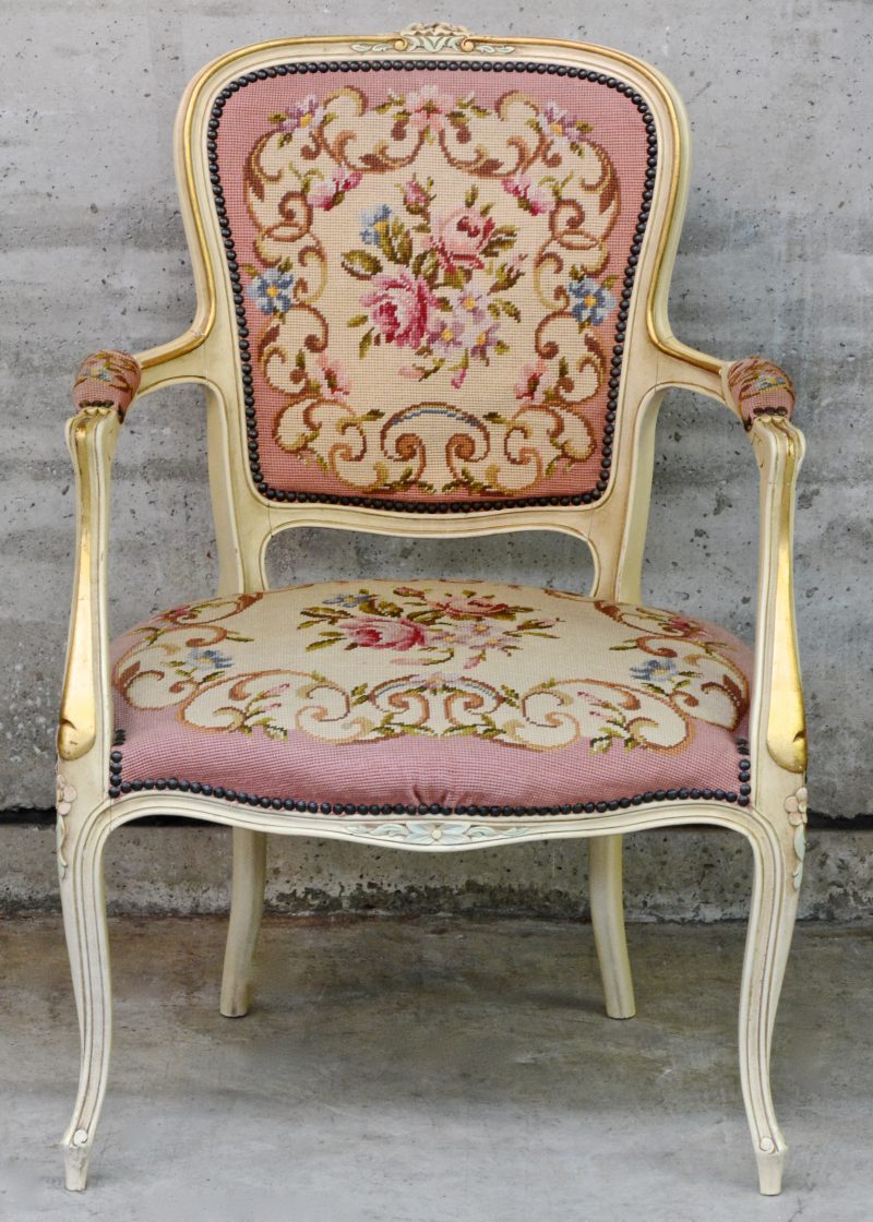 Een fauteuil en cabriolet van woitgepatineerd hout met vergulde en gepolychromeerde details en bekleed met naaldwerk.