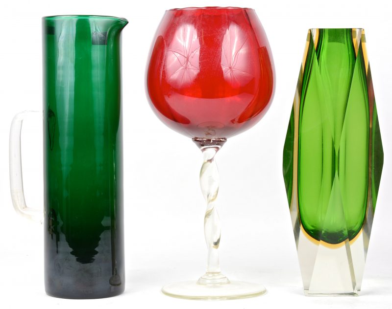 Een lot kristal en glaswerk, bestaande uit een geslepen groene vaas, een langerekte groene kan en een rood sierglas op voet.