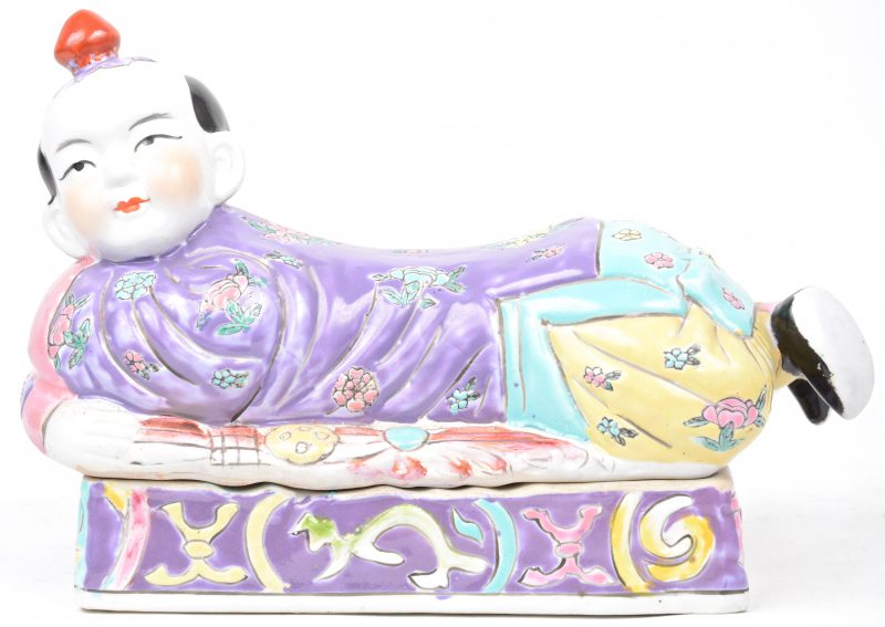 Een Chinese neksteun/dekseldoos in van meerkleurig porselein in de vorm van een liggend kind.