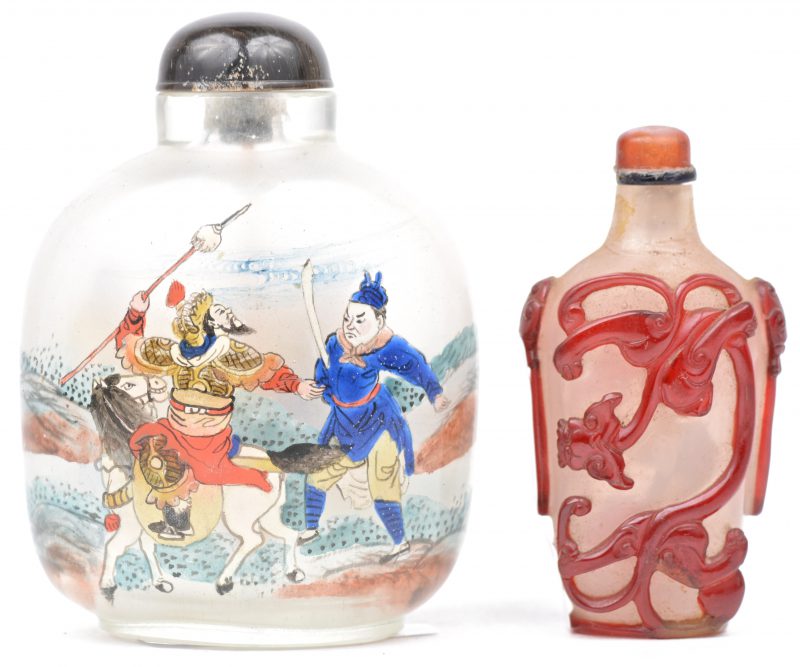 Twee glazen snuffbottles, waarbij één met een rood reliëfdecor van een draak, en het andere met een handgeschilderd decor van krijgers.