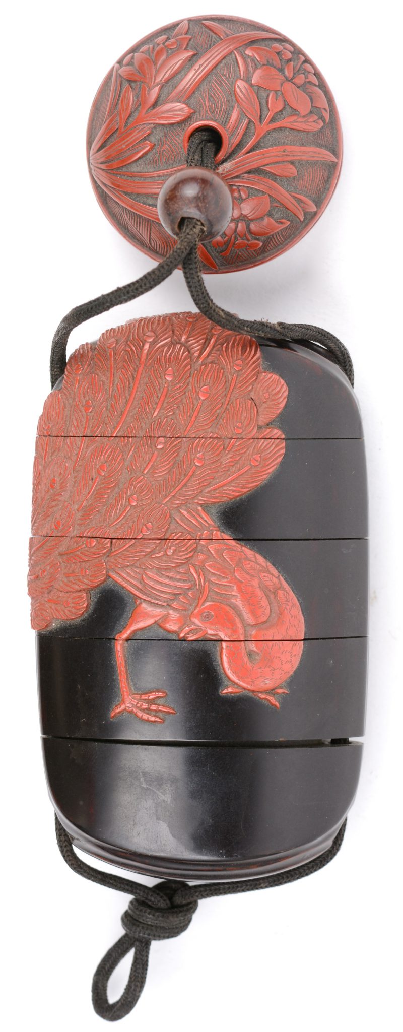 Een Inro-doosje van zwartgelakt bamboe, versierd met een pauwendecor van rode lak en een knoop met een reliëfdecor van bleoemen. Japan, begin XXe eeuw.