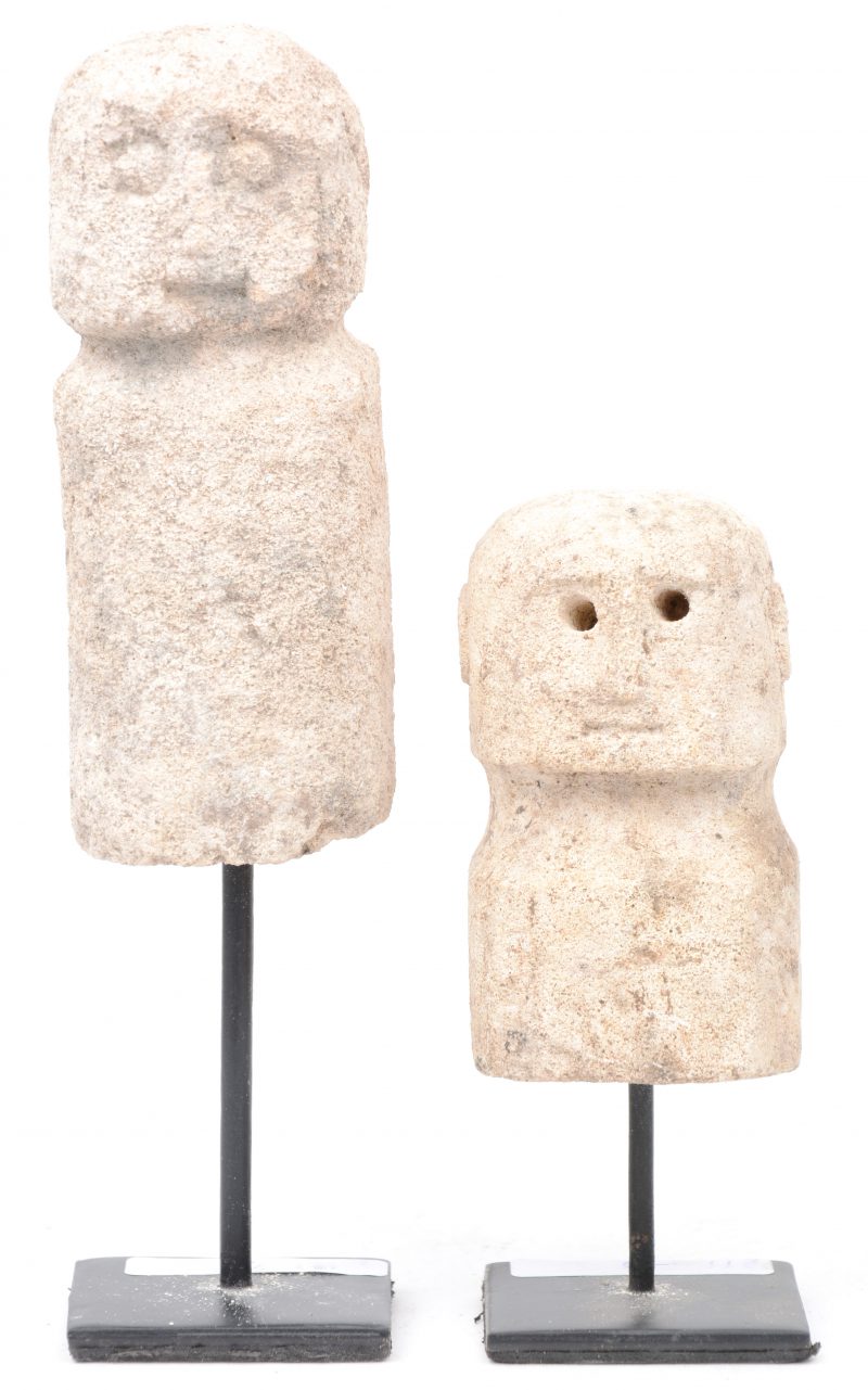 Twee figuurtjes van gebeeldhouwd steen op metalen sokkeltjes.
