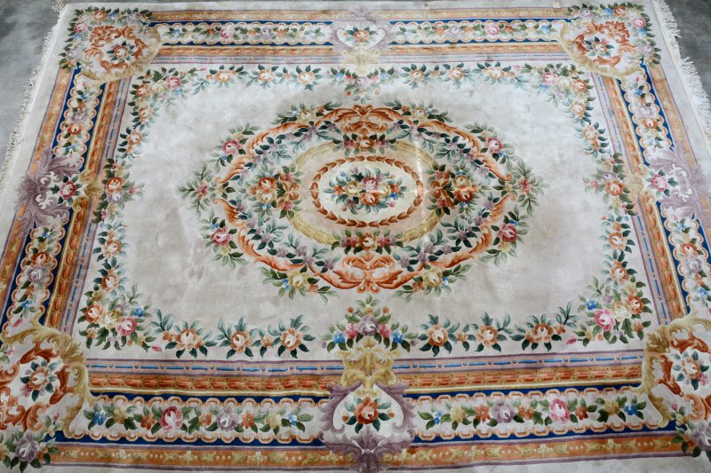 Een Chinees wollen tapijt met bloemenmotieven. Twee beschadigingen van meubelpoten.