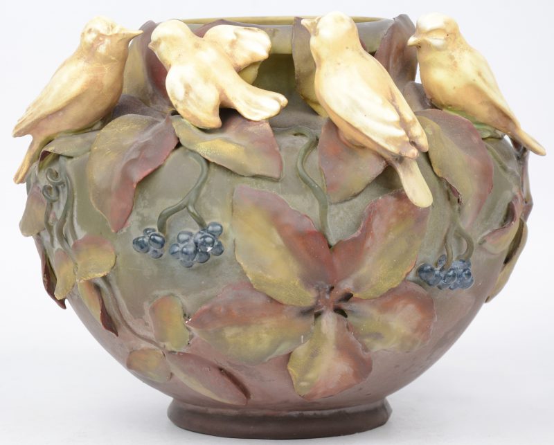 Een vaas van meerkleurig aardewerk, versierd met bladeren, bessen en vier vogeltjes in hoogreliëf. Eén snaveltje licht beschadigd.