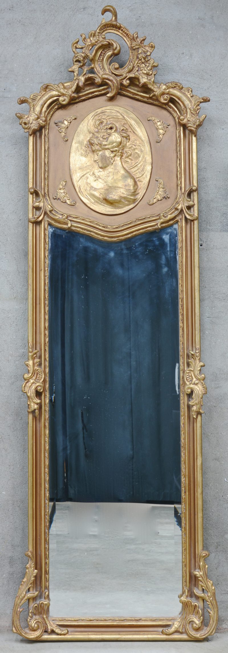 Een vergulde spiegel in Lodewijl XV-stijl met een vrouwenbuste in een medaillon en een rocaille in de kuif.