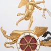 Een vergulde schouwpendule met een reliëfdecor van classicistische figuren met een strijdwagen. De pendule als wiel van een strijdwagen met tweespan, versierd met een draak en bestuurd door een engel.