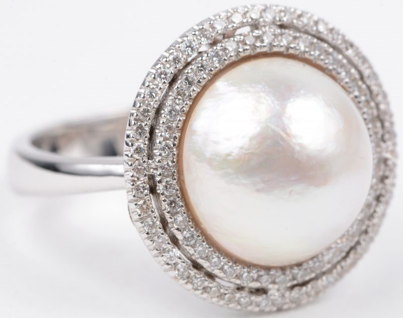 Een 18 karaats wit gouden ring bezet met diamanten met een gezamenlijk gewicht van ± 0,44 ct. en een centrale parel van Ø 1,50 cm.