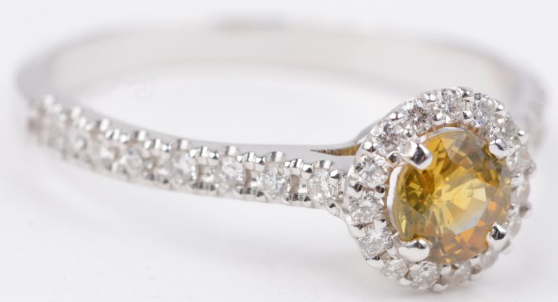 Een 18 karaats wit gouden ring bezet met diamanten met een gezamenlijk gewicht van ± 0,25 ct. en een gele saffier van ± 0,40 ct.