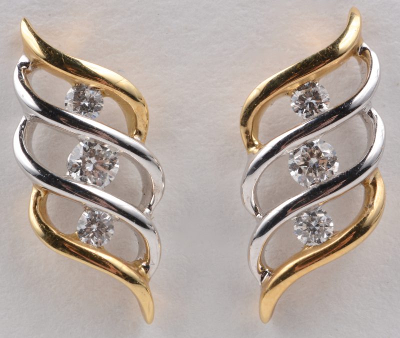 Een paar 18 karaats wit en geel gouden oorbellen bezet met diamanten met een gezamenlijk gewicht van ± 0,28 ct.