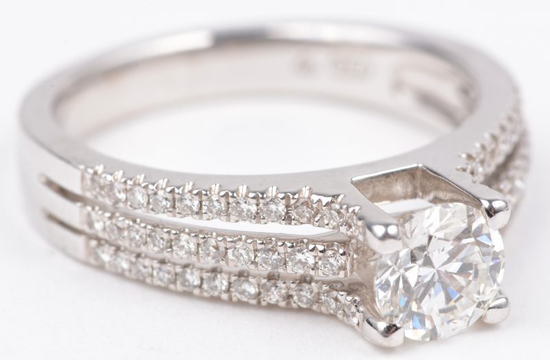 Een 18 karaats wit gouden ring bezet met een centrale diamant van ± 0,72 ct. VVS1 en drie rijen briljanten met een gezamenlijk gewicht van ± 0,34 ct.