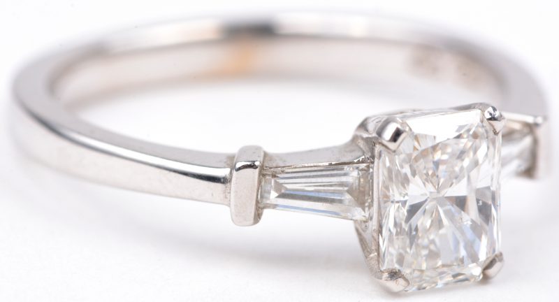 Een 18 karaats wit gouden ring met bezet met een centrale diamant emerald cut van ± 0,90 ct. en twee diamant baguettes met een gezamenlijk gewicht van ± 0,20 ct.