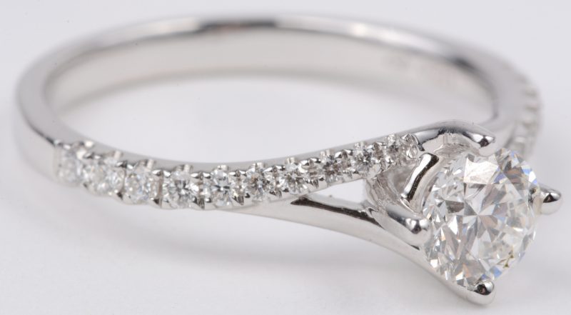 Een 18 karaats wit gouden ring met bezet een centrale diamant van ± 0,60 ct. VVS1 en briljanten met een gezamenlijk gewicht van ± 0,20 ct.