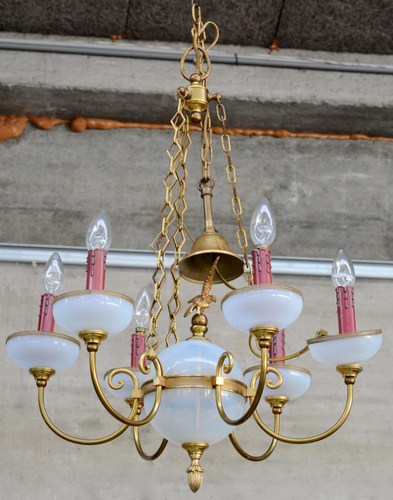 Een kleine kroonluchter van koper en opaalglas. Met zes lichtarmen en een centrale bol versierd met een arend.