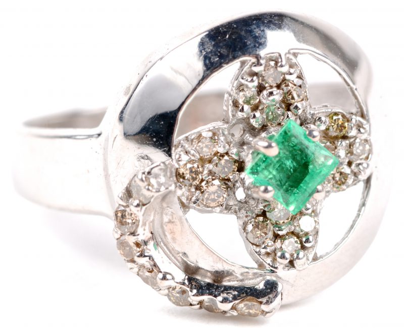 Een 18 karaats wit gouden ring bezet met briljanten met een gezamenlijk gewicht van ± 0,20 ct. eb een centrale smaragd van ± 0,15 ct.