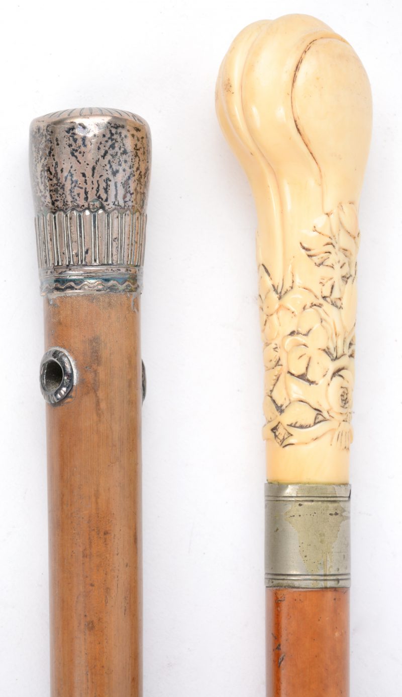 Een houten wandelstok met 800‰ zilveren handvat en een tweede met een handvat van ivorine, versierd met een bloemendecor in reliëf.