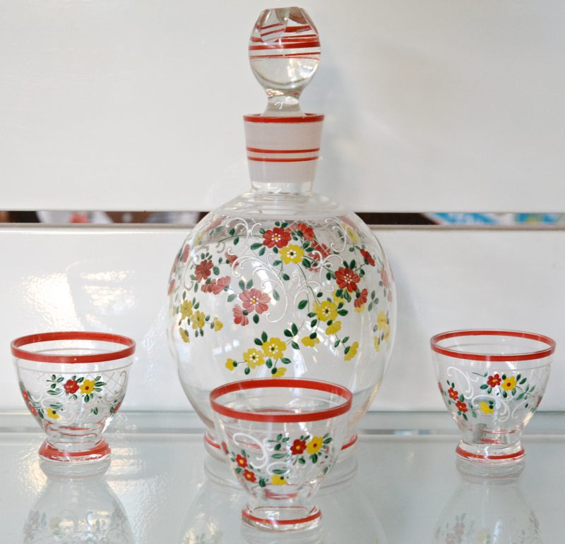 Een bol glazen karafje met drie bijpassende glaasjes met handgeschilderde decors. Omstreeks 1900.