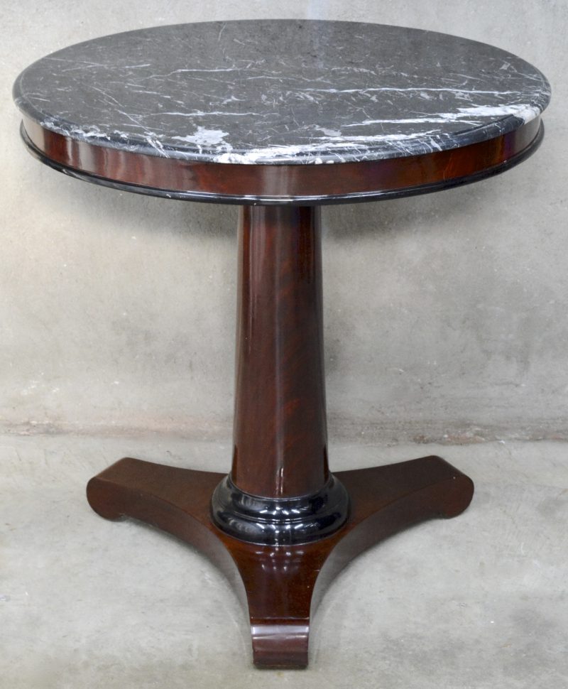 Een ronde notenhouten tafel in Empirestijl met een zwart marmeren blad.