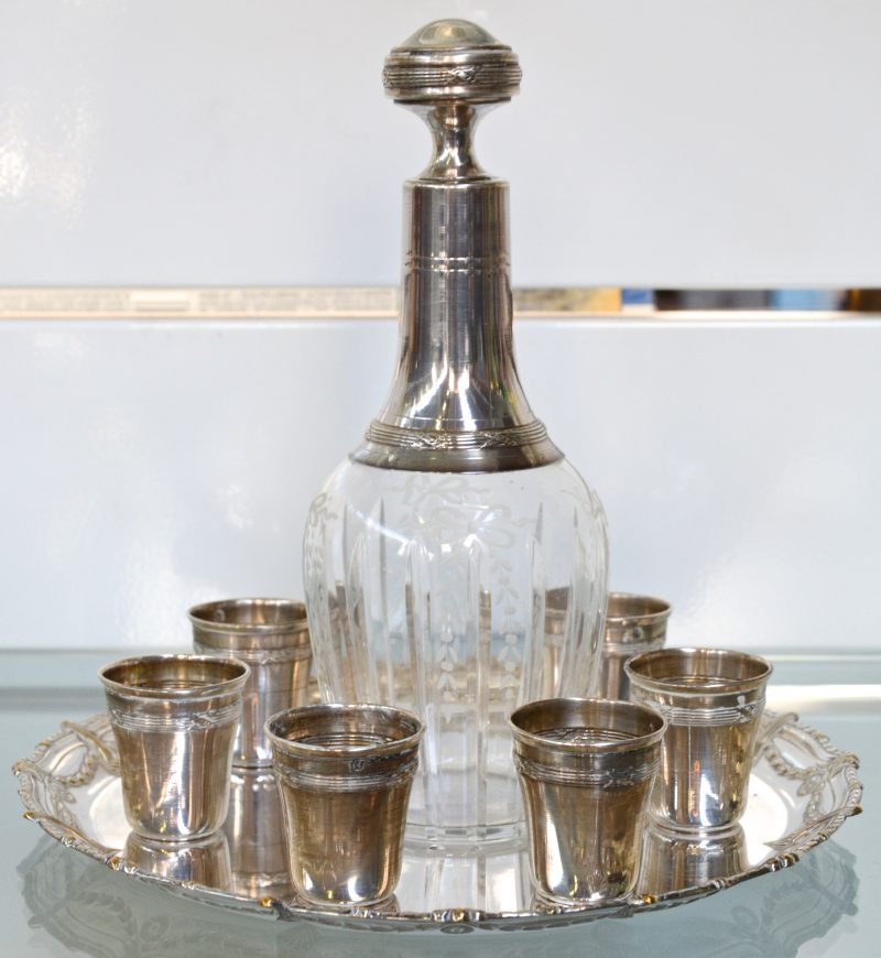 Een likeurkaraf in geslepen en gegraveerd kristal met zilveren montuur en zes kleine zilveren  gobelets, samen op verzilverd schaaltje van WMF.