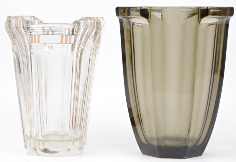 Twee verschillende kristallen vazen, waarbij één kleurloze met vergulde motieven en de andere van rookbruin kristal.