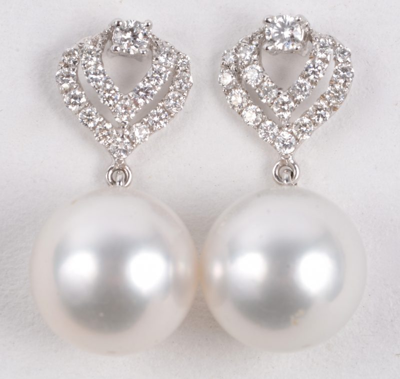 Een paar 18 karaats wit gouden oorbellen bezet met diamanten met een gezamenlijk gewicht van ± 0,42 ct. En twee parels.