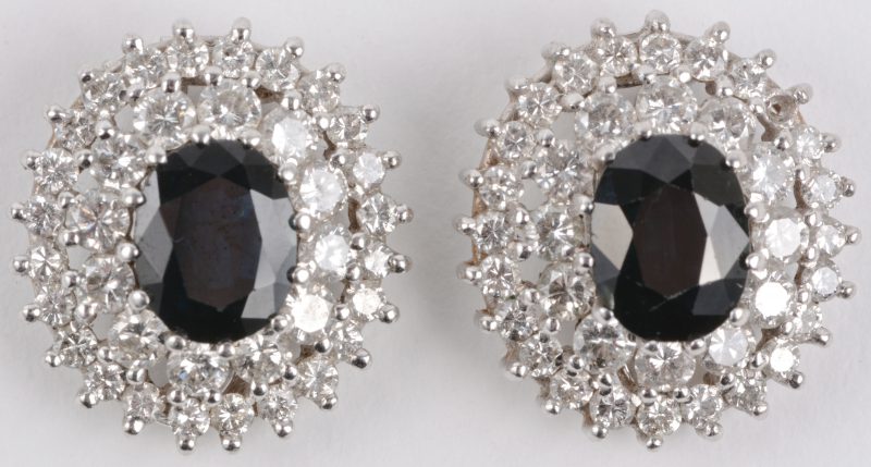 Een paar 18 karaats wit gouden oorbellen bezet met diamanten met een gezamenlijk gewicht van ± 3 ct. en telkens een centrale saffier van ± 2 ct.