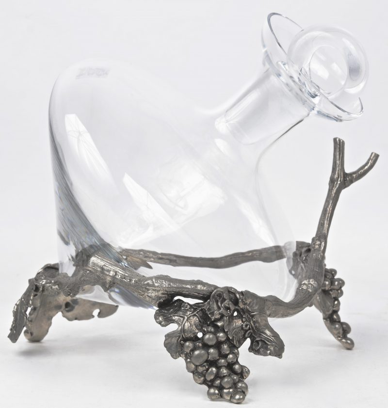 Een glazen decanteur in een metalen houder in de vorm van druivenranken.