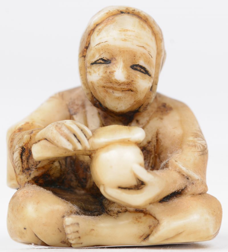 Een antieke Japanse netsuke van gesculpteerd ivoor ion de vorm van een zittende man. Onderaan gesigneerd.