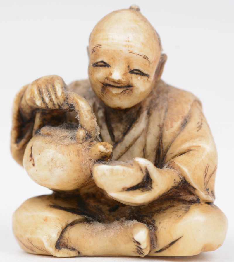 Een antieke Japanse netsuke van gesculpteerd ivoor ion de vorm van een zittende man met theepot. Onderaan gesigneerd.