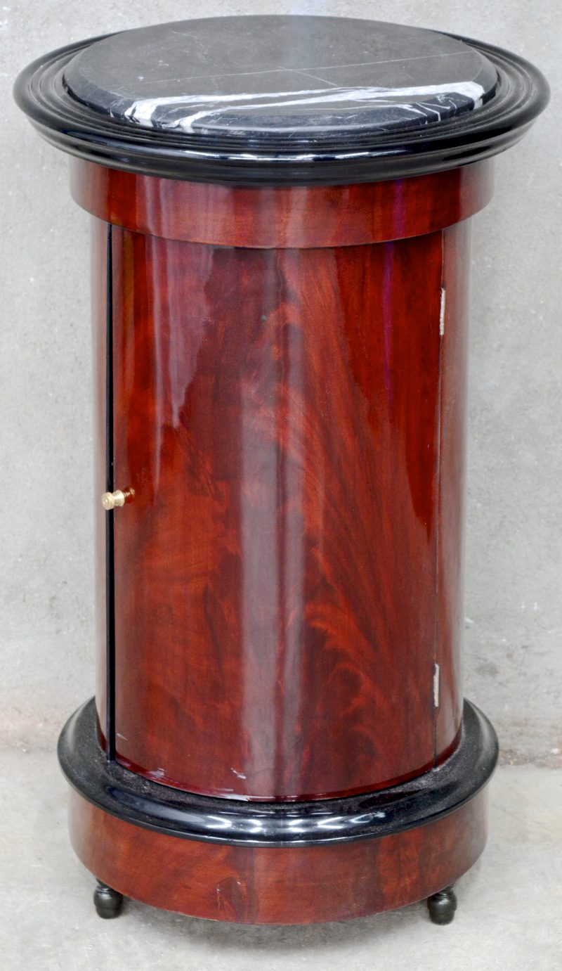 Een rond bijzetkastje van mahoniehoutfineer met één lade en een zwart marmeren blad.