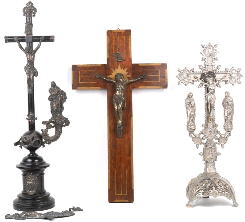Een verzilverd metalen staand kruisbeeld en een kruisbeeld van verzilverd metaal en zwart perenhout (beschadigd). We voegen er een wandkruisbeeld aan toe.