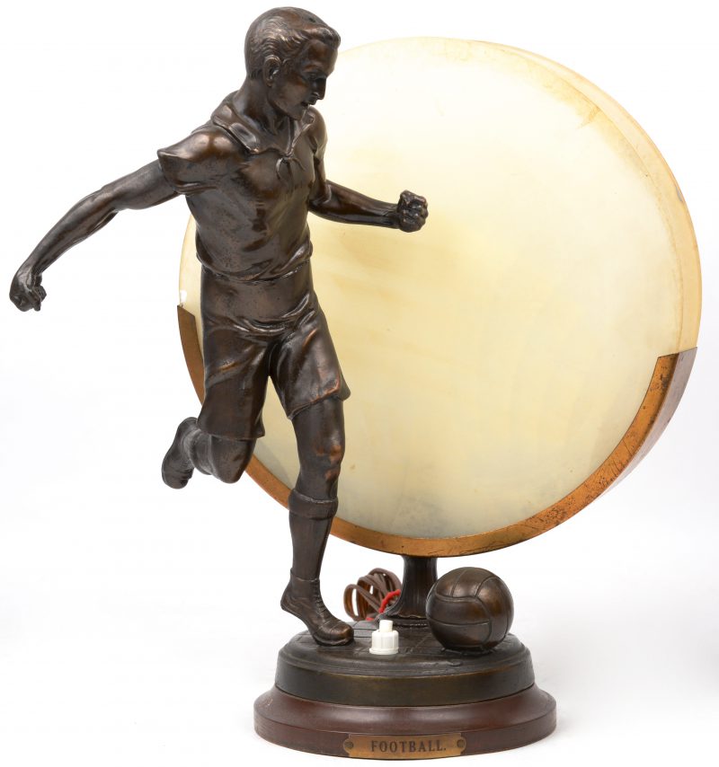 Een art deco schemerlampje van zamac en gegivreerd glas met voorstelling van een voetballer.