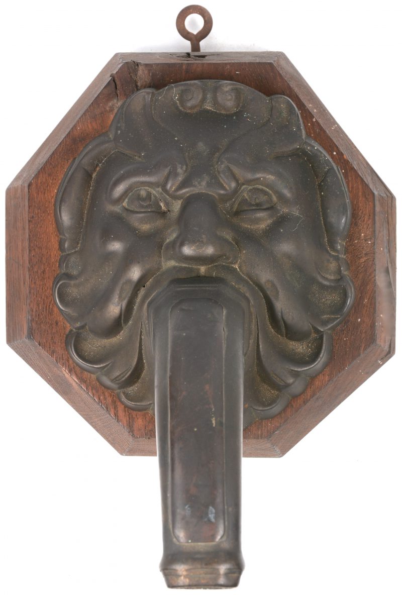 Een barokke waterspuwer van brons. Op houten wandplaquette.