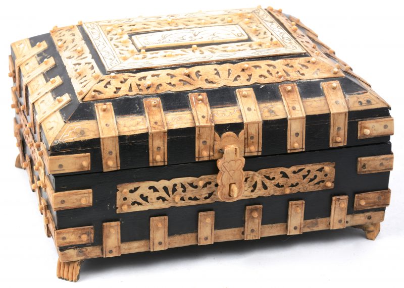 Een kistje van zwartgelakt hout met mansardevormig deksel, versierd met gesculpteerd benen oplegwerk.