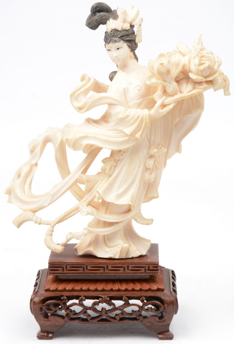 “Geisha met bloemstuk”. Een beeldje van fijn gesculpteerd ivoor op een houten voetstuk.