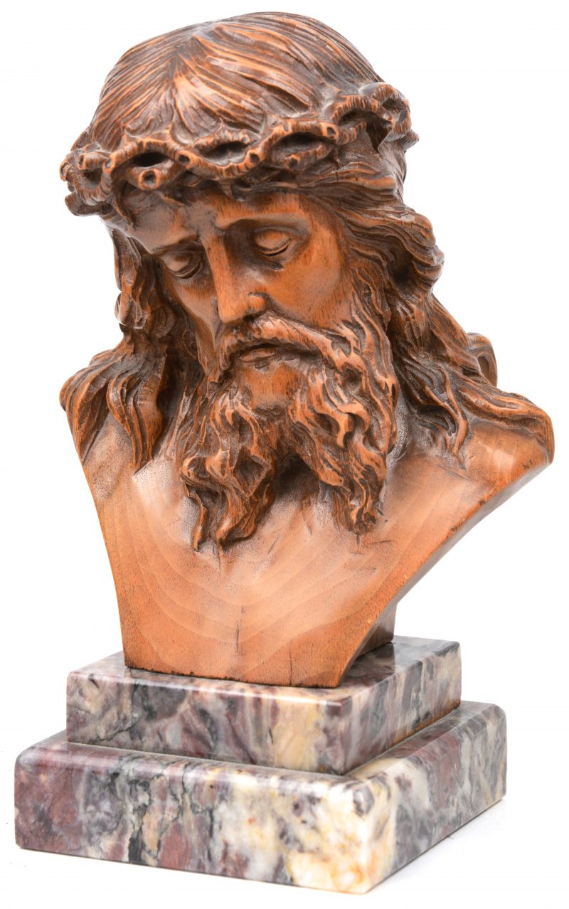 Een gesculpteerde houten buste van Christus op marmeren sokkel.