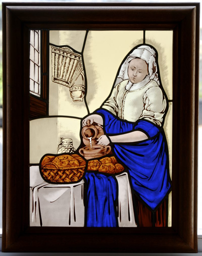“Het melkmeisje van Vermeer”. Glasraam in smeedijzeren omlijsting. Met verlichting.