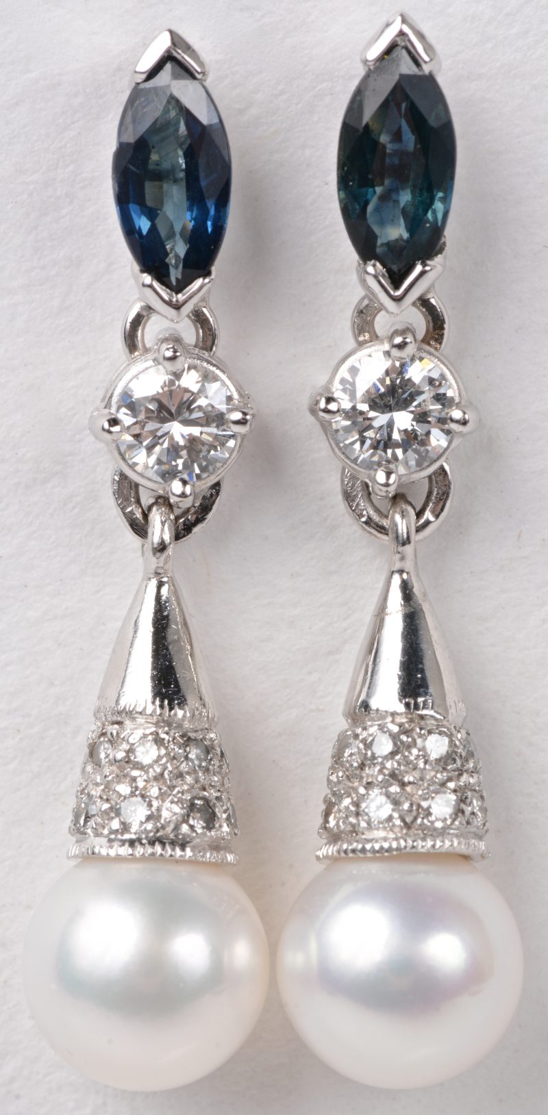 Een paar 18 karaats wit gouden oorbellen bezet met twee parels, diamanten met een gezamenlijk gewicht van ± 0,30 ct. en twee saffieren van ± 0,20 ct.
